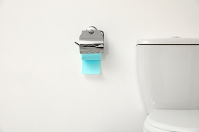 Holder with toilet paper roll on white wall in bathroom