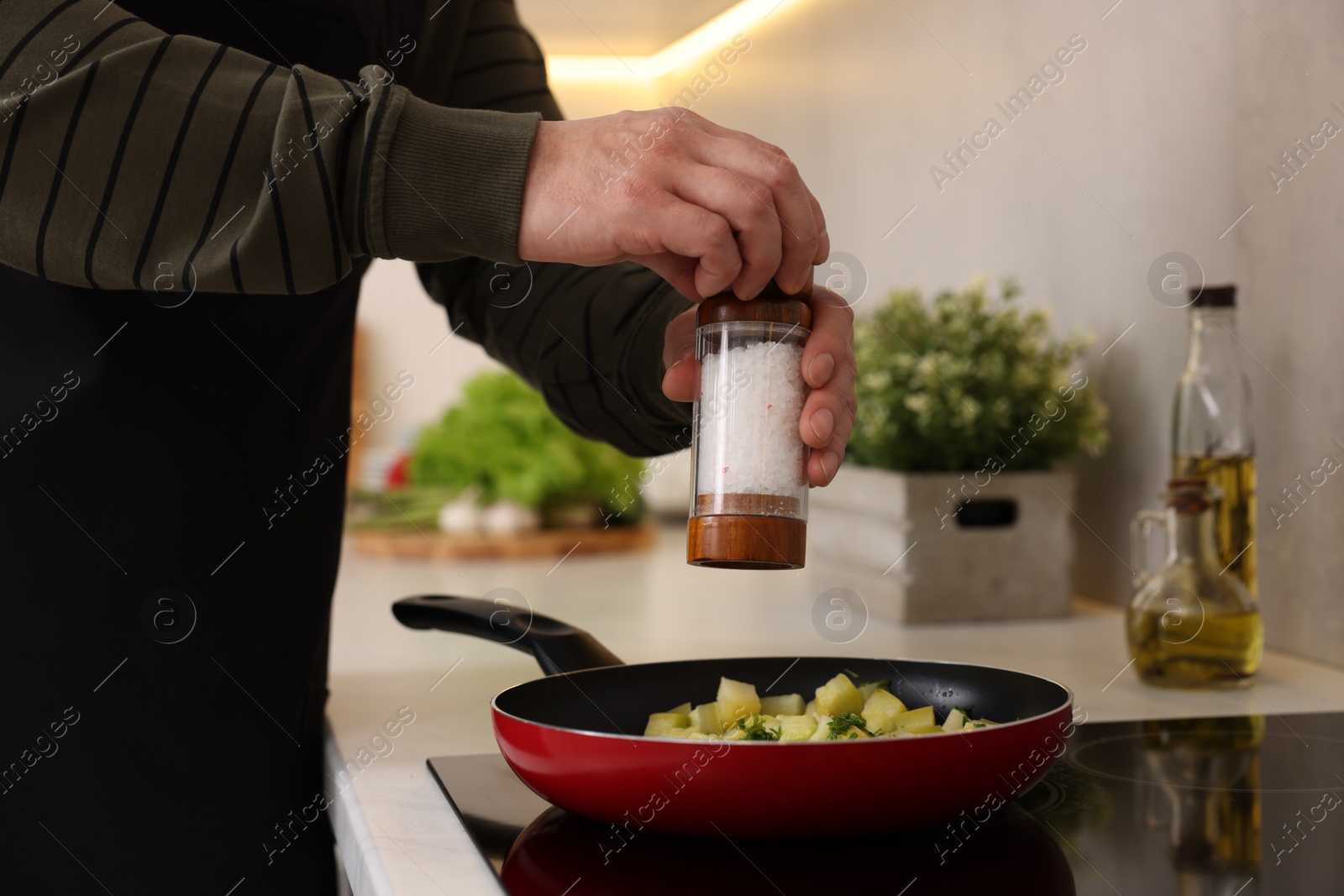 Photo of Cooking process. Man adding salt into frying pan in kitchen, closeup