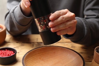 Photo of Woman grinding pepper with shaker at wooden table, closeup