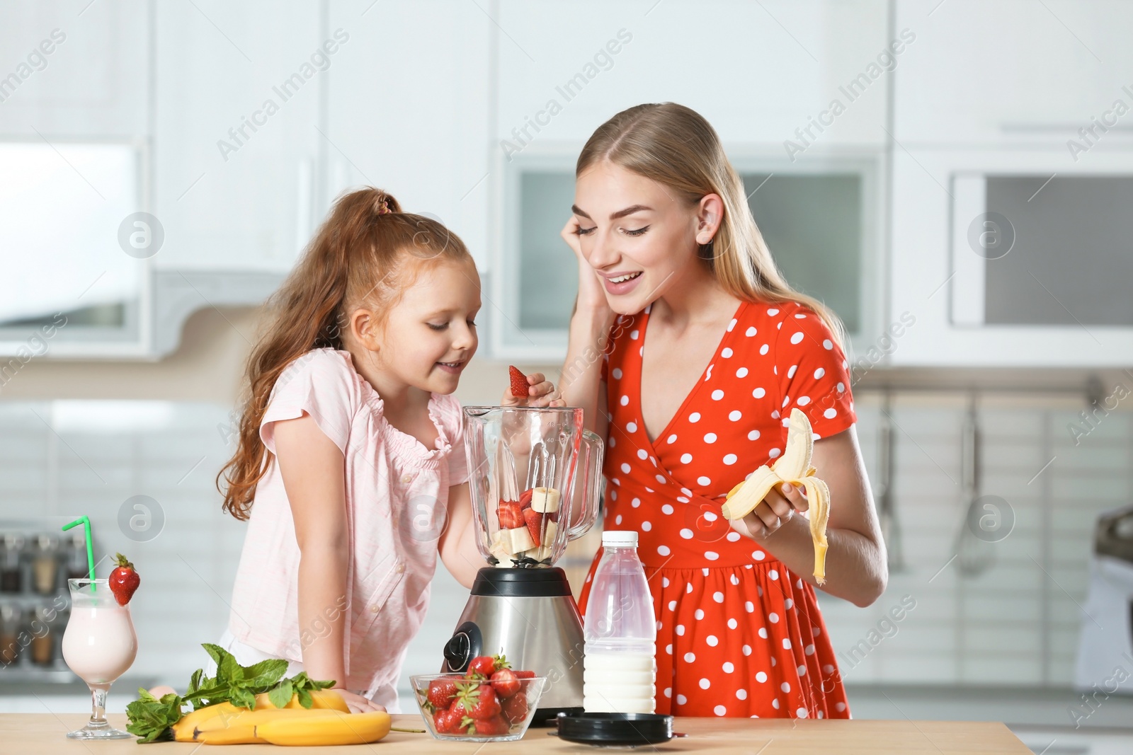 Photo of Mother and daughter preparing delicious milk shake in kitchen