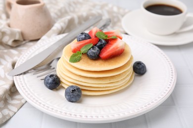 Photo of Delicious pancakes with strawberries, blueberries and mint on white tiled table, closeup