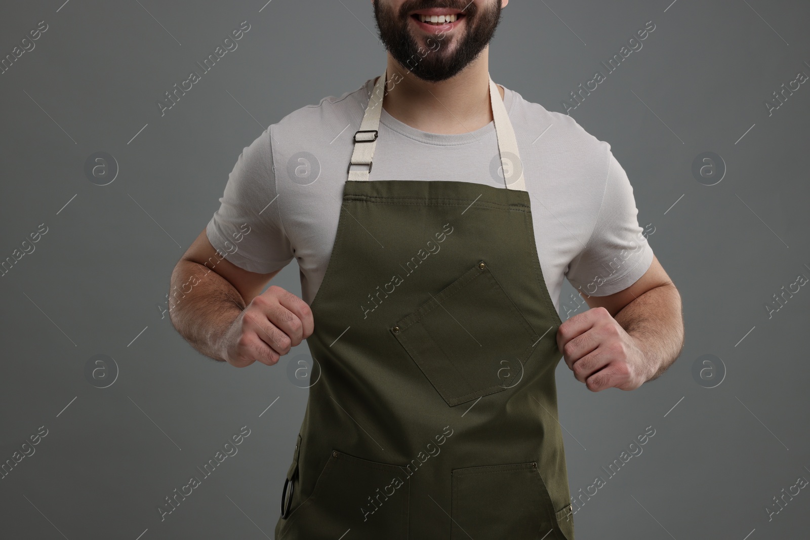 Photo of Smiling man in kitchen apron on grey background, closeup. Mockup for design