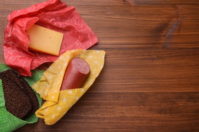 Photo of Different products in beeswax food wraps on wooden table, flat lay. Space for text