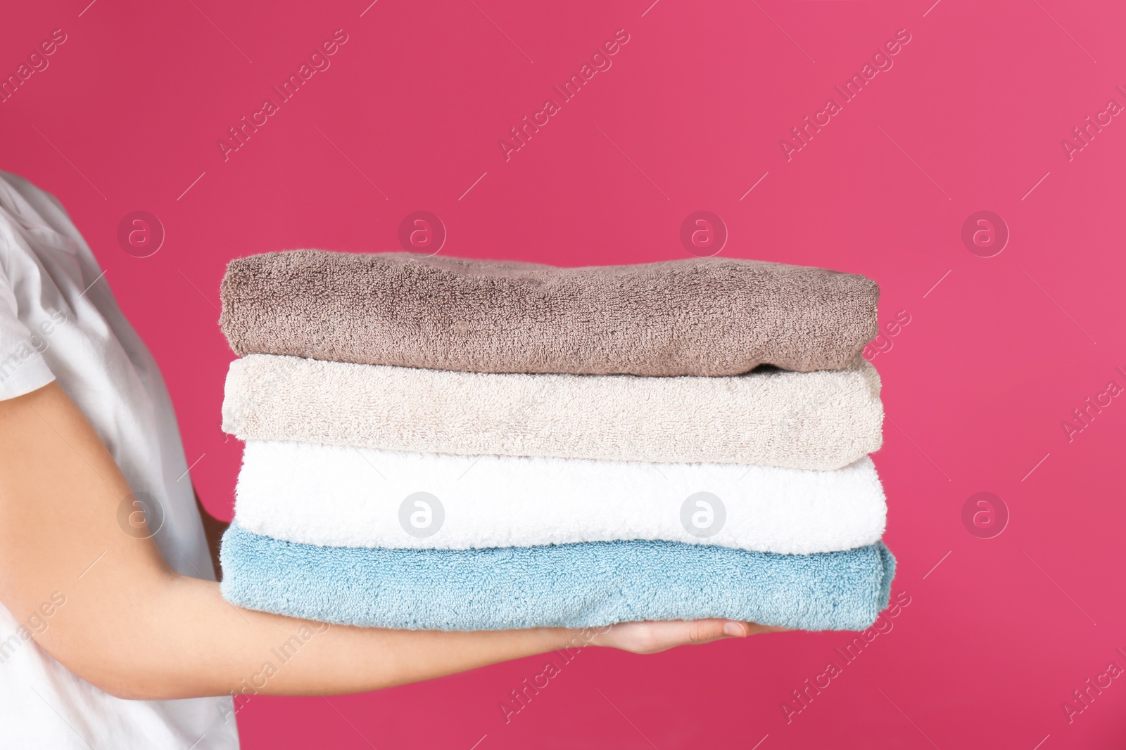 Photo of Young woman holding clean towels on color background, closeup. Laundry day