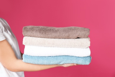 Young woman holding clean towels on color background, closeup. Laundry day