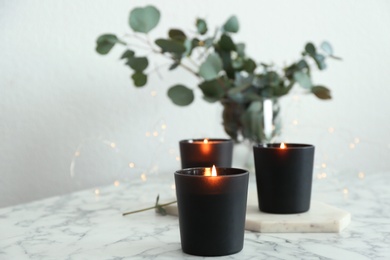 Photo of Burning candles and green branches with fairy lights on marble table