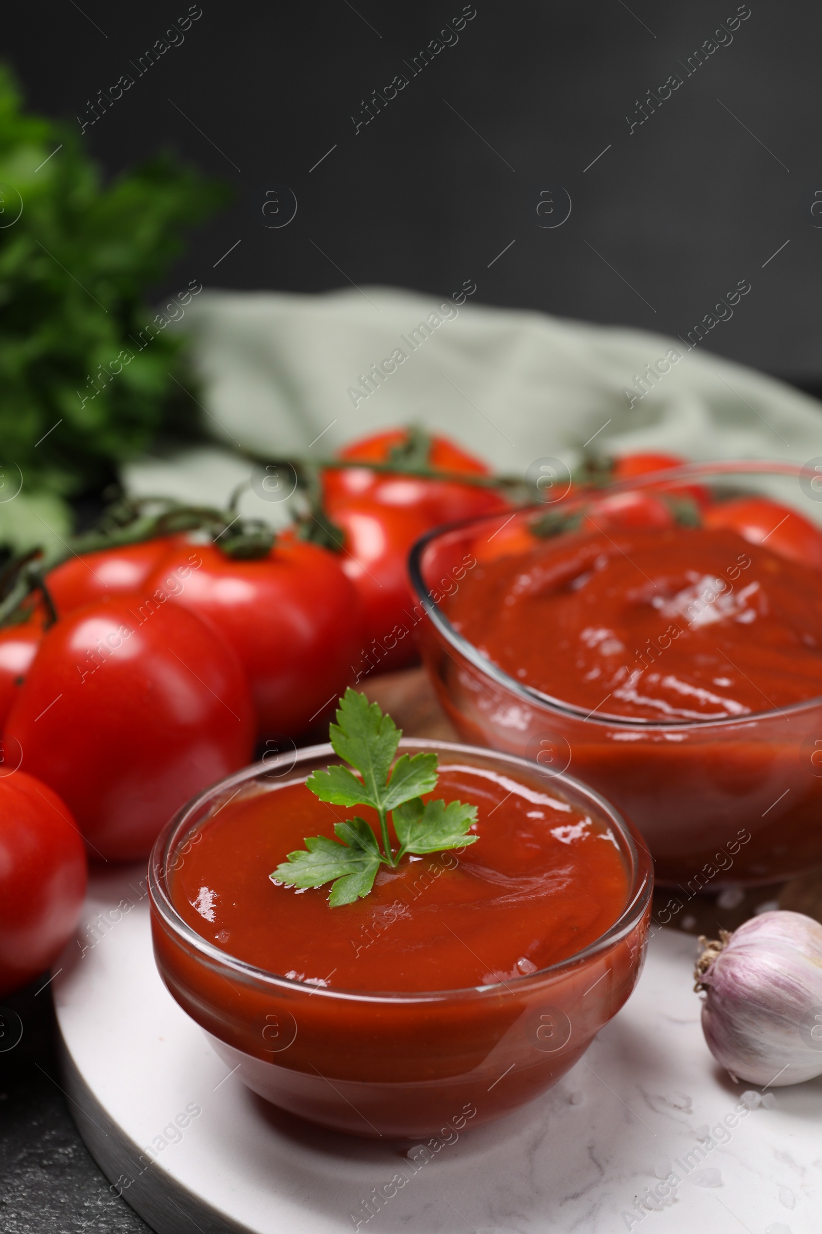 Photo of Organic ketchup in bowls and fresh tomatoes on table, closeup. Tomato sauce