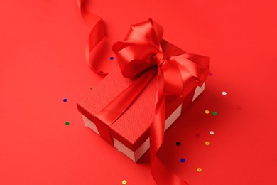 Beautiful gift box with bow and confetti on red background