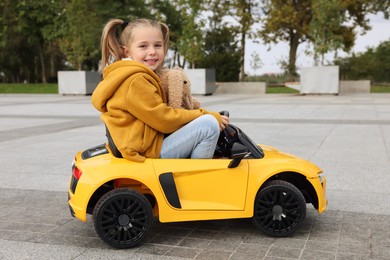 Cute little girl with toy bunny driving children's car on city street