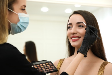 Photo of Professional makeup artist working with client in salon. Beauty services during Coronavirus quarantine