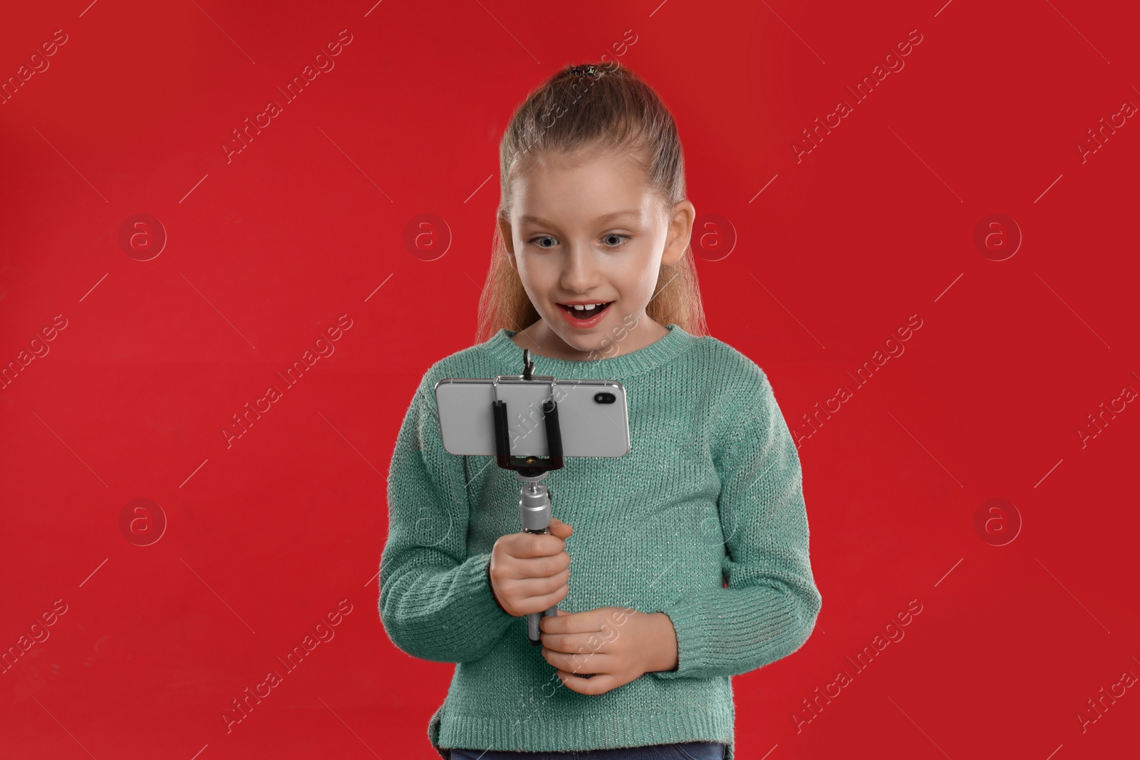 Photo of Surprised little blogger recording video on red background