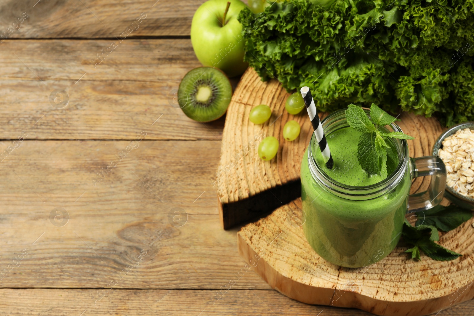 Photo of Mason jar of fresh green smoothie and ingredients on wooden table, space for text