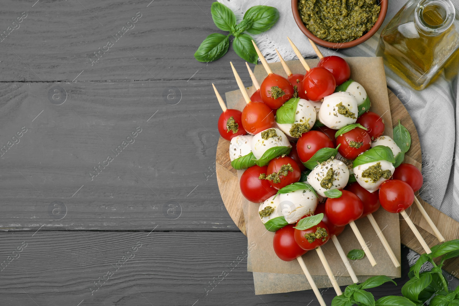 Photo of Caprese skewers with tomatoes, mozzarella balls and basil on grey wooden table, flat lay. Space for text