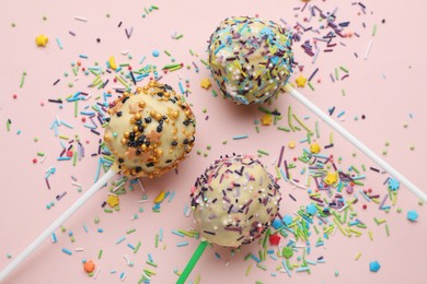 Photo of Delicious confectionery. Sweet cake pops decorated with sprinkles on pale pink background, flat lay