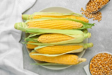 Photo of Plate of fresh corncobs and kernels on grey table, flat lay