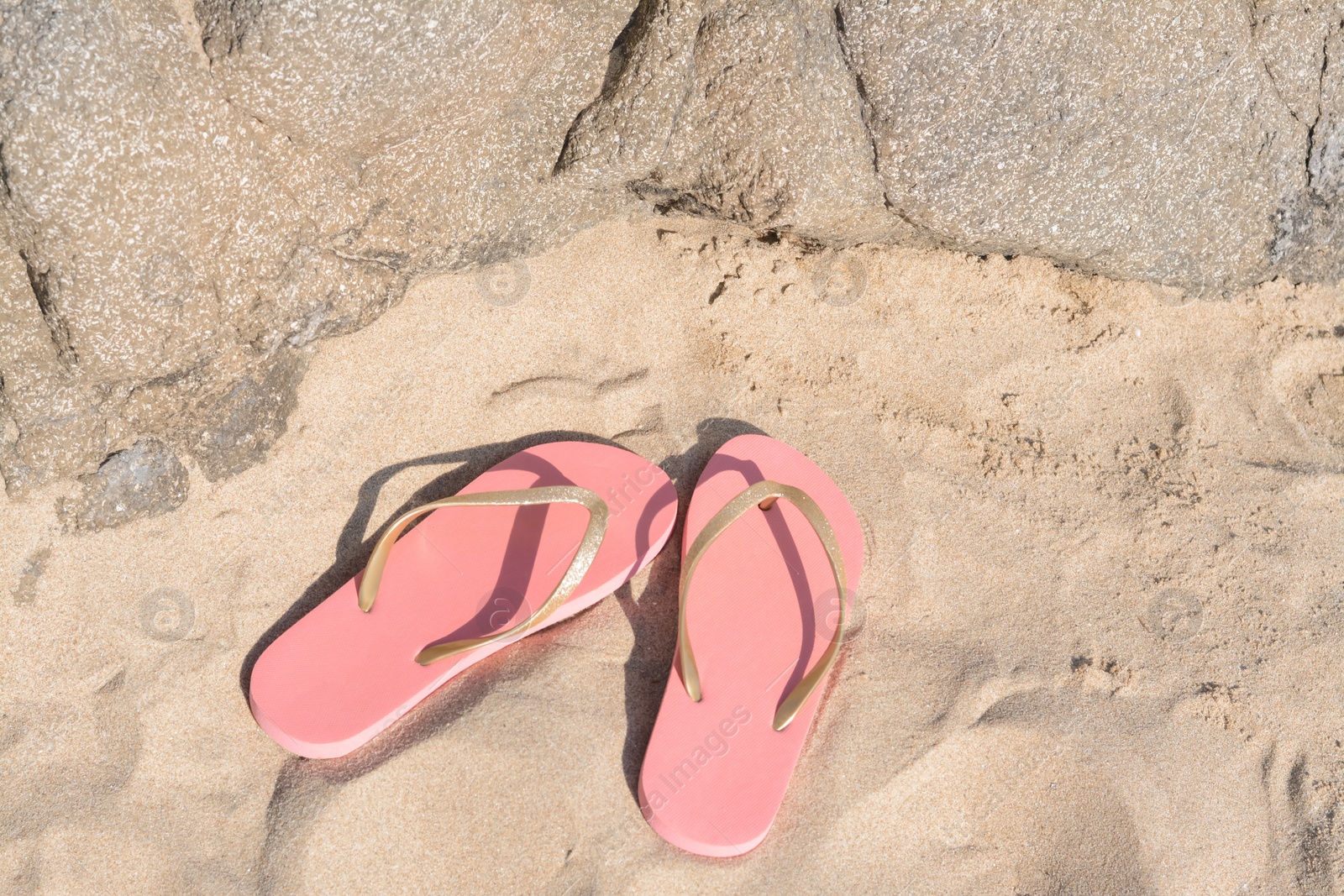 Photo of Stylish pink flip flops on sandy beach near rock, above view
