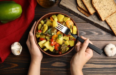 Photo of Woman eating delicious dish with potatoes from earthenware at wooden table, top view