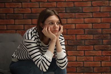 Photo of Sad young woman sitting on chair near brick wall, space for text