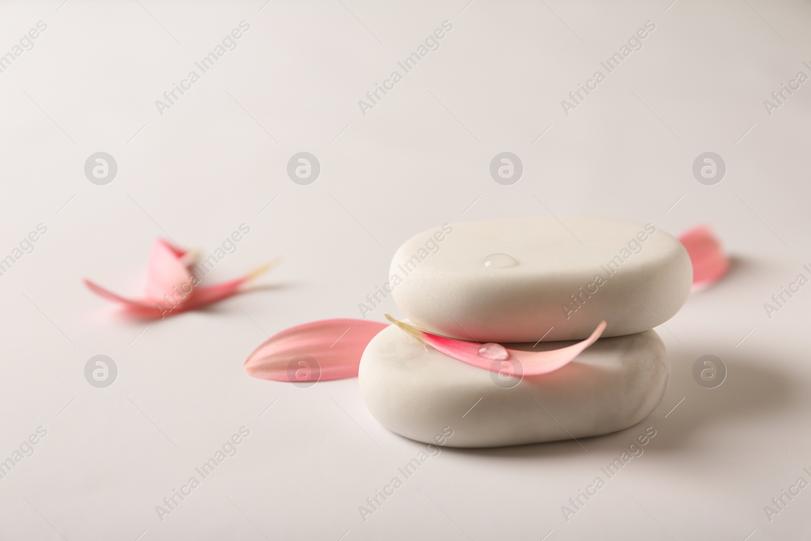 Photo of Stacked spa stones with flower petals on light background. Space for text