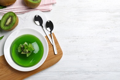 Photo of Delicious green jelly with kiwi slices on white wooden table, flat lay. Space for text