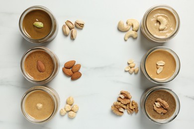 Tasty nut butters in jars and raw nuts on white marble table, flat lay