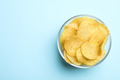 Delicious crispy potato chips in bowl on color background, top view with space for text