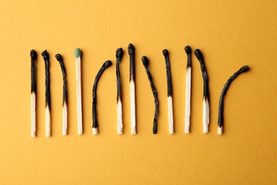Photo of Row of burnt matches and whole one on color background, flat lay. Uniqueness concept