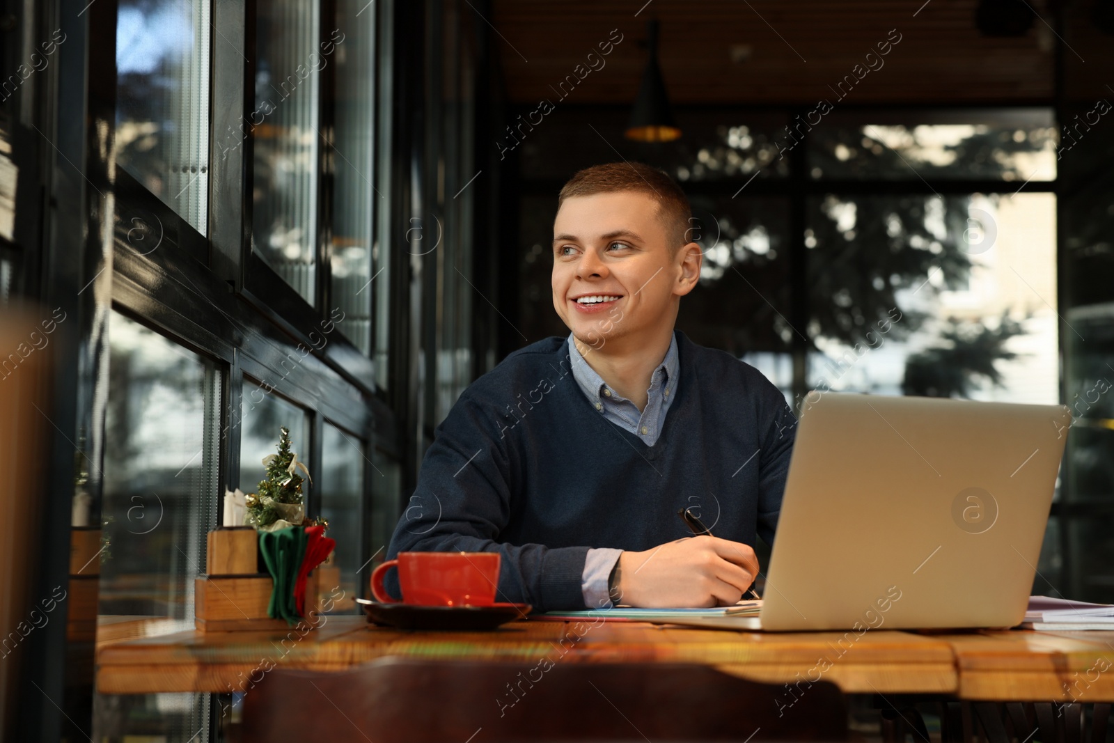 Photo of Young male student with laptop studying at table in cafe