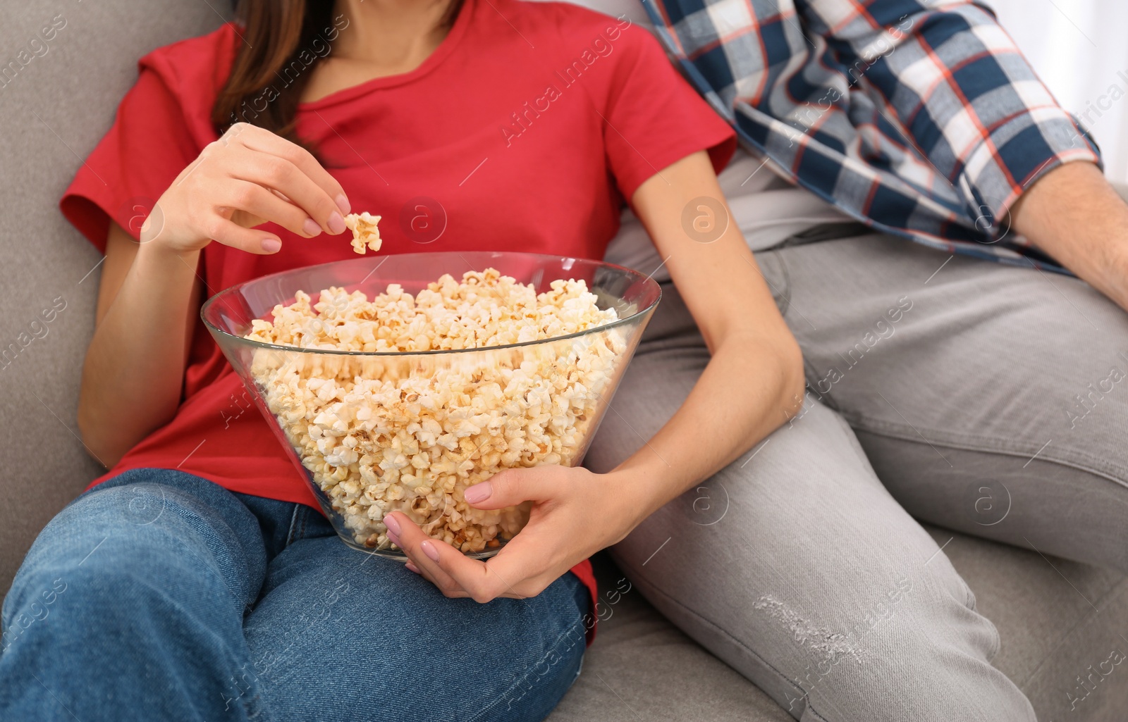 Photo of Young couple watching TV with popcorn on sofa at home