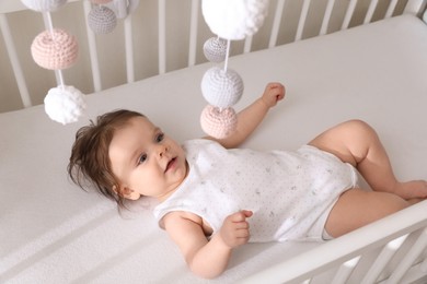 Cute little baby lying in crib with hanging mobile