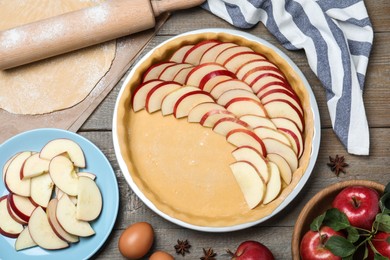 Photo of Dish with fresh apple slices and raw dough on wooden table, flat lay. Baking pie