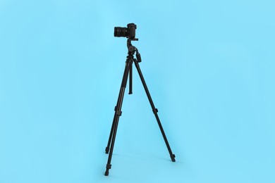 Modern tripod with professional camera on light blue background
