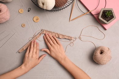 Woman knitting with threads at grey table, top view. Engaging hobby