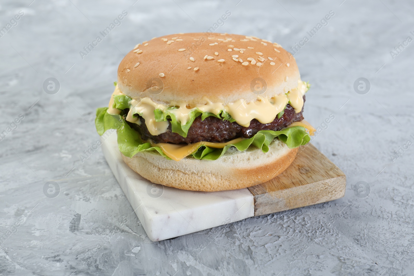 Photo of Delicious cheeseburger on grey textured table, closeup