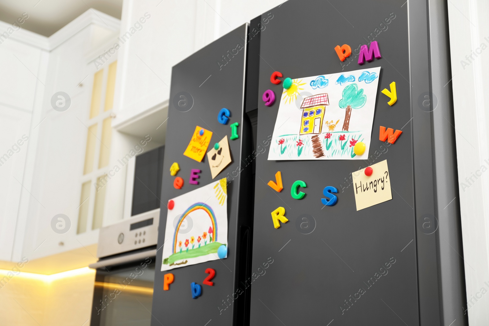 Photo of Modern refrigerator with child's drawings, notes and magnets in kitchen