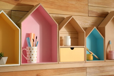 Photo of Painted house shaped shelves with different items on wooden wall. Interior elements