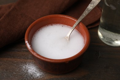 Photo of Chemical reaction of vinegar and baking soda in bowl on wooden table, closeup