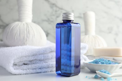 Photo of Spa composition. Bottle of cosmetic product, sea salt, towel, soap and herbal bags on white table