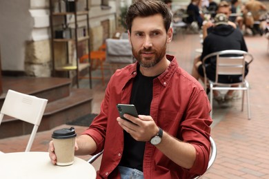 Photo of Handsome bearded man with coffee and smartphone in outdoor cafe