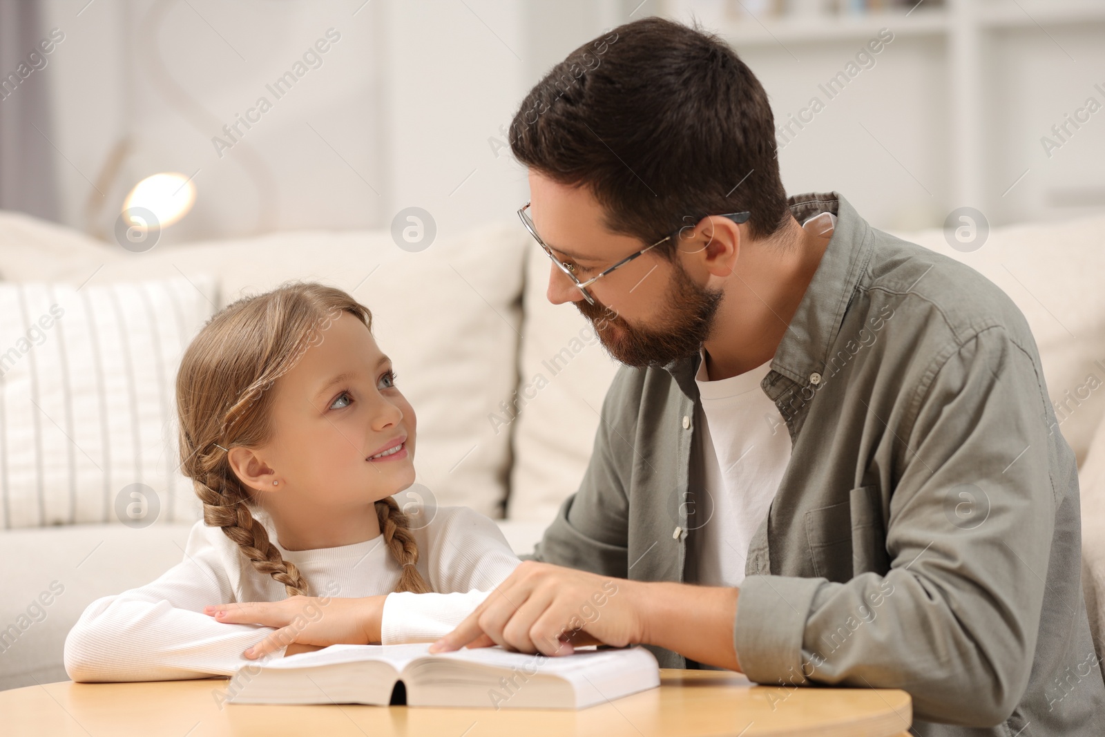 Photo of Girl and her godparent reading Bible together at table in room