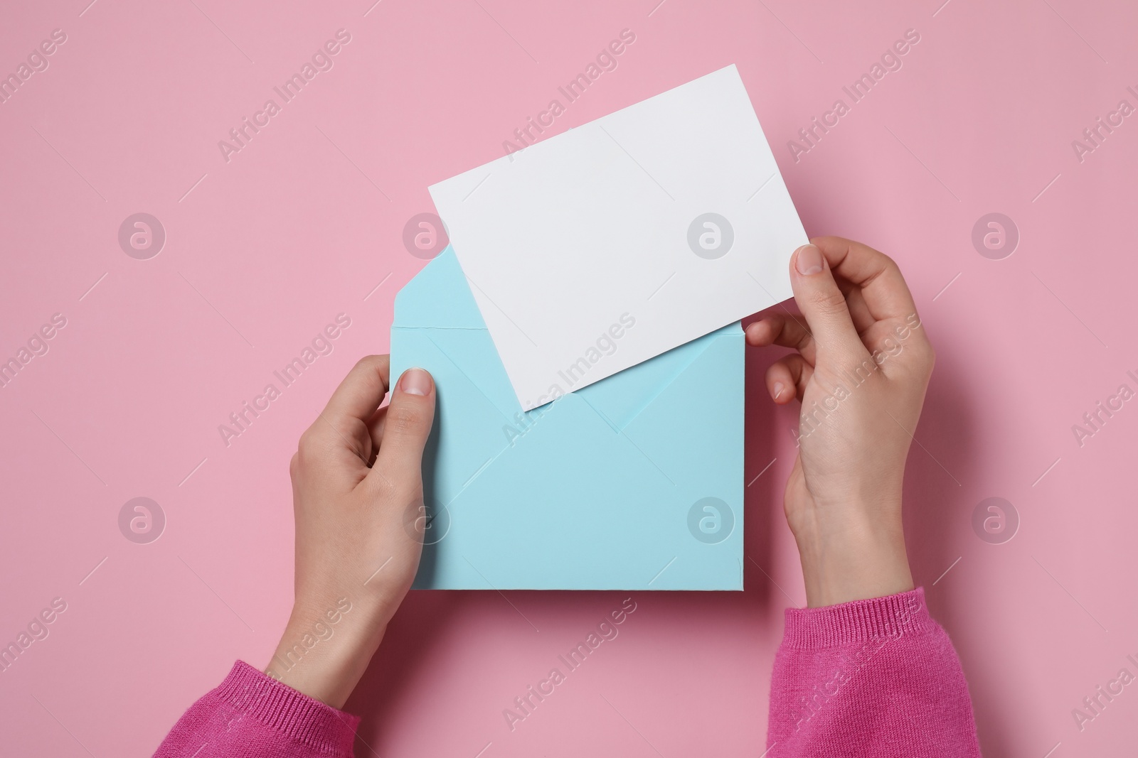 Photo of Woman taking card out of letter envelope at pink table, top view. Space for text