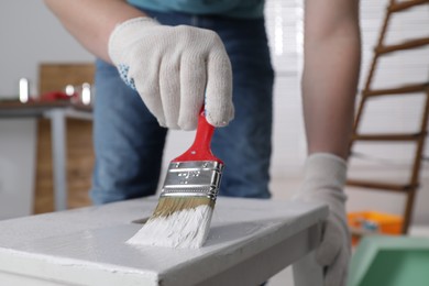 Photo of Man using brush to paint bekvam with white dye indoors, closeup