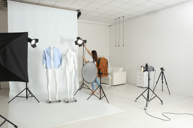 Photo of Ghost mannequins with modern clothes and professional photographer fixing lighting in photo studio