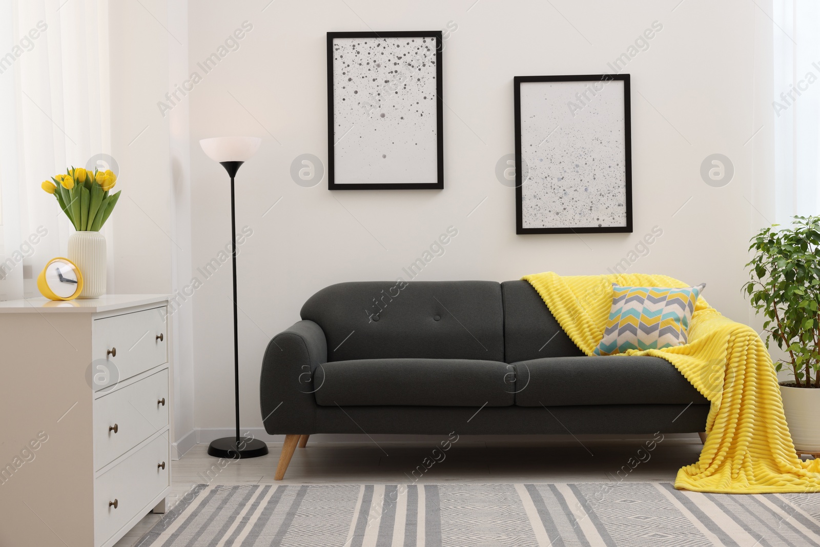 Photo of Spring atmosphere. Stylish living room interior with comfortable furniture and bouquet of beautiful yellow tulips