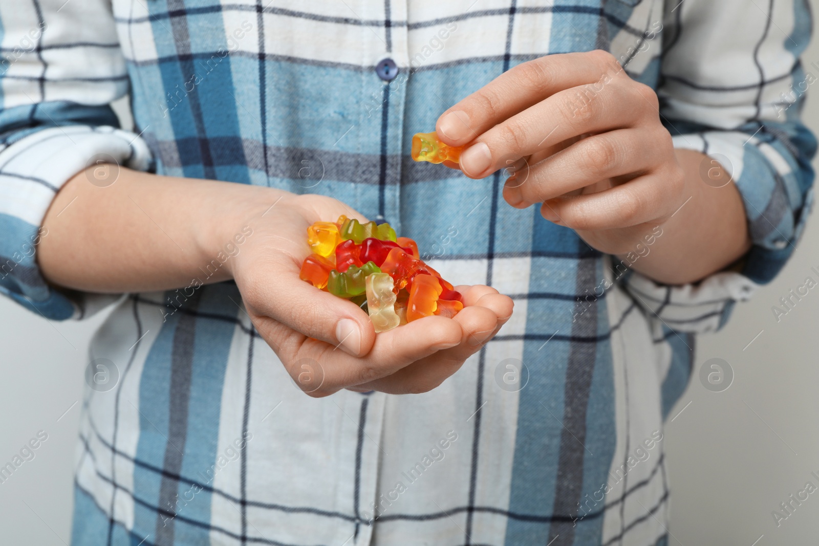 Photo of Woman holding colorful jelly bears on light background, closeup