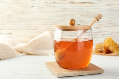 Glass jar with sweet honey and dipper on table. Space for text