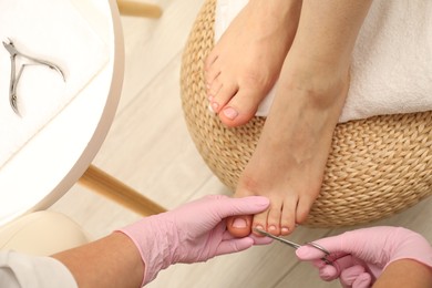Photo of Professional pedicurist cutting client`s toenails with scissors in beauty salon, closeup