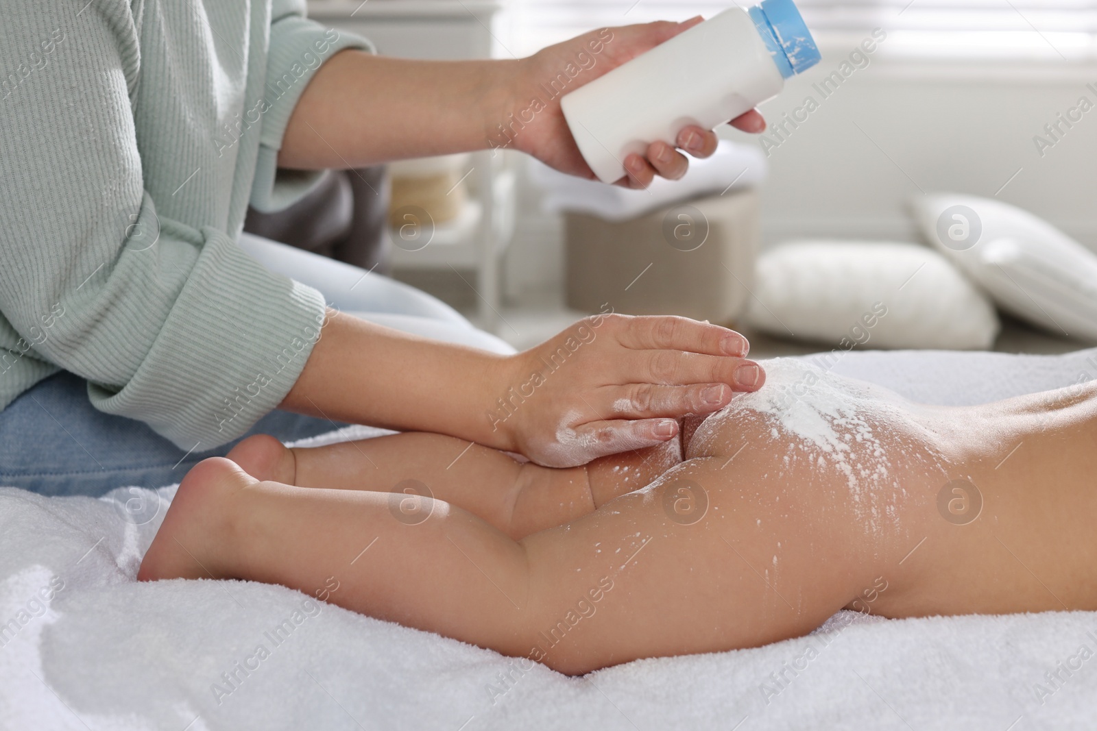 Photo of Mother applying dusting powder on her baby at home, closeup