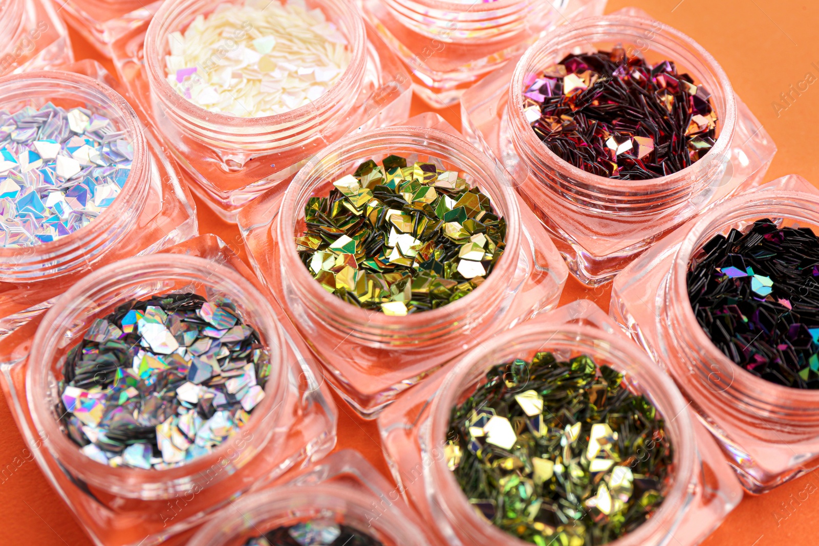 Photo of Jars with colorful shiny glitter on orange background, closeup