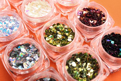 Jars with colorful shiny glitter on orange background, closeup